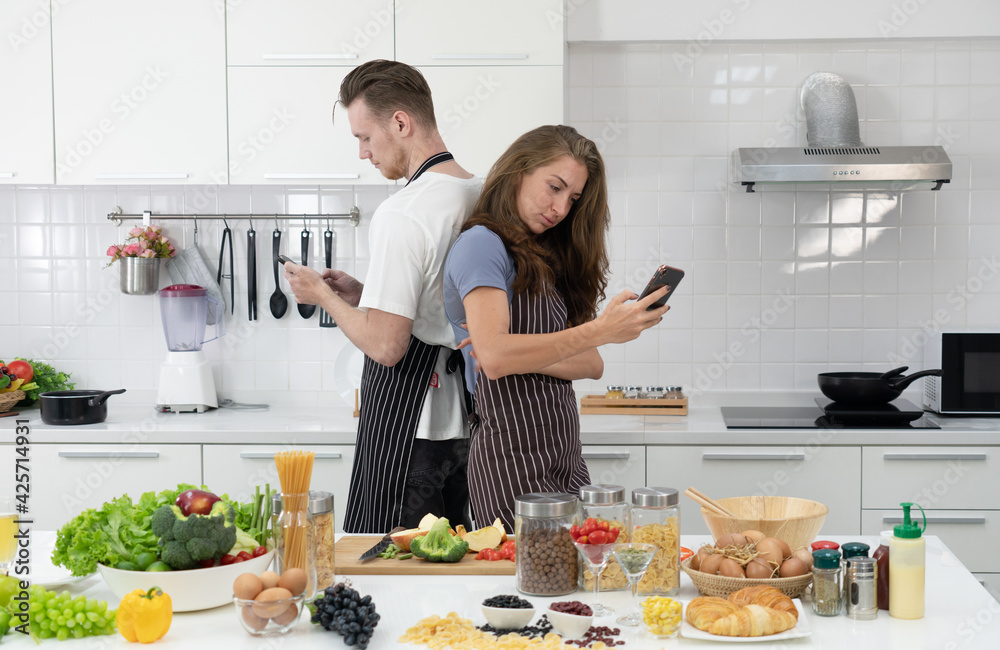 young caucasian couple using smartphone while cooking healthy food for breakfast. togetherness concept
