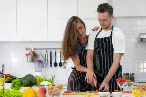 young woman holding hand of the man to chop vegetable to prepare lunch in kitchen. couple together concept