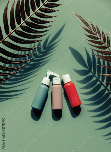 Three bottles with shampoo  lotion and cream green background with palm leaves