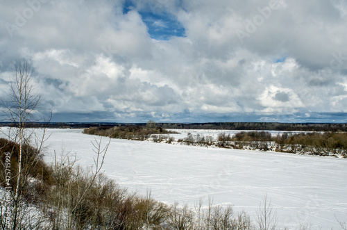 Winter landscape with a high bank of the river covered with ice  cumulus clouds in the sky .deep snow cover with footprints  a clear horizon line.