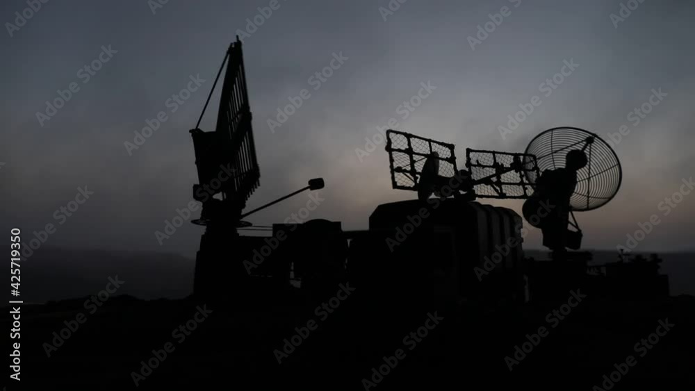 Creative artwork decoration. Silhouette of mobile air defence truck with radar antenna during sunset. Rocket launcher aimed at sky ready to attack. Selective focus
