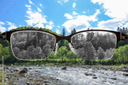 Looking through glasses to black and white river and forest landscape focused in women's glasses. Color blindness. World perception during depression. Medical condition. Health and disease concept. photo