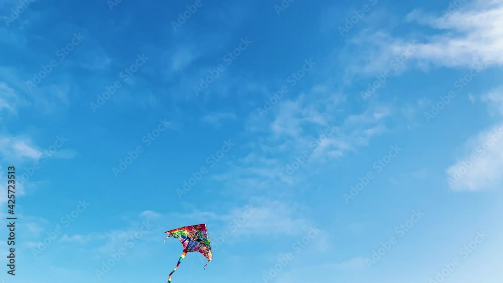 Flight of bright kite against the blue joyful sky with white clouds