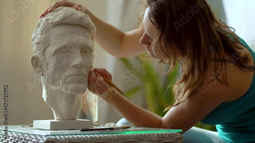 Sculptor repairing gypsum sculpture of man's head. Woman working in studio
