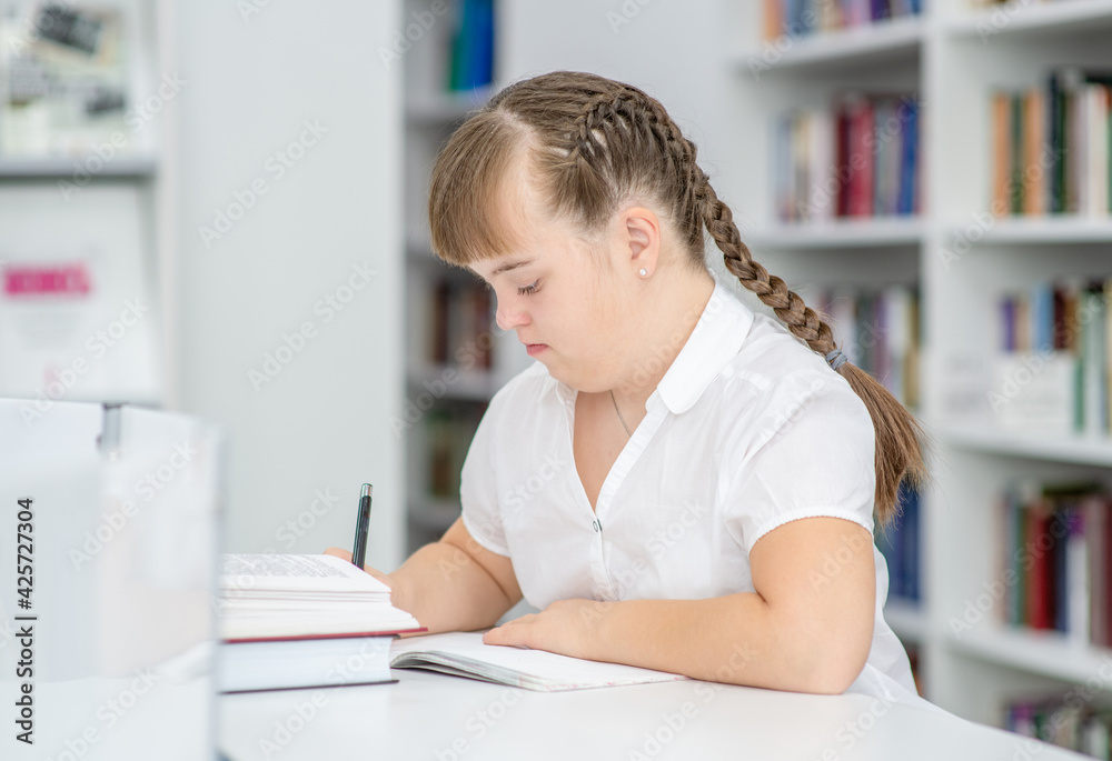 Young girl with down syndrome doing homework at home. Education for disabled children concept Young girl with down syndrome doing homework at home. Education for disabled children concept