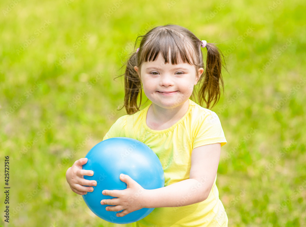 Smiling little girl with syndrome down holds ball in a summer park Smiling little girl with syndrome down holds ball in a summer park