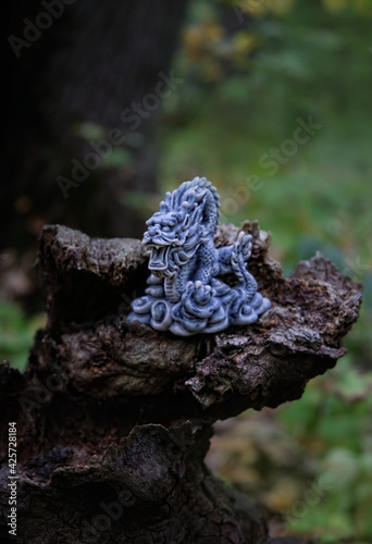 asian dragon statue on old tree trunk, natural forest background. beautiful stone dragon, symbol of wisdom, good start, Imperial power, deity. Fabulous atmosphere mystery witchcraft composition