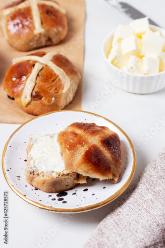 Fresh homemade Traditional Easter treats hot Cross Buns with raisins, served with butter and knife on marble bench top