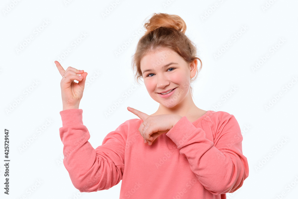 Cute young girl in pink casual sweatshirt pointing fingers aside. Smiling at camera. White studio background Cute young girl in pink casual sweatshirt pointing fingers aside. Smiling at camera. White studio background