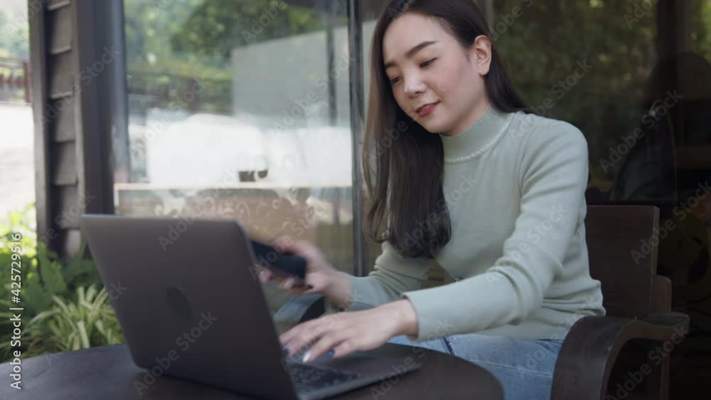 Asian woman freelance talking on mobile phone while typing on laptop in coffee shop. Asian woman freelance talking on mobile phone while typing on laptop in coffee shop.