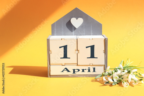 Календарь на 11 апреля : кубики с цифрами 0 и 11, название месяца Апрель на английском языке, букет цветущих подснежников на желтом фоне на солнце и в тени предметов photo