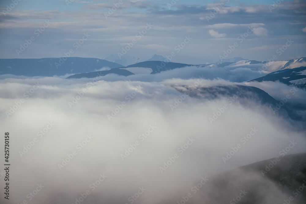 Awesome mountain landscape with sharp snowy mountain peak on horizon above clouds. Atmospheric minimal alpine scenery with pointed pinnacle above many low clouds. Cloudy sea, cloudy ocean in mountains