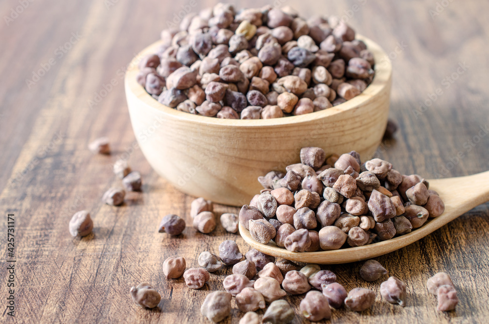 Dry organic brown chickpea seeds in wooden bowl and spoon on table background for clean food or agricultural product concept Dry organic brown chickpea seeds in wooden bowl and spoon on table background for clean food or agricultural product concept