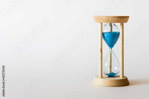 Falling blue sand in a sand clock on white background. Photo with copy blank space. 