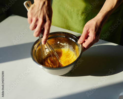Homemade cakes baking, Easter pie preparing or cookie concept. Chef in green apron mixing sugar and eggs in a metal bowl using wire whisk. High quality photo