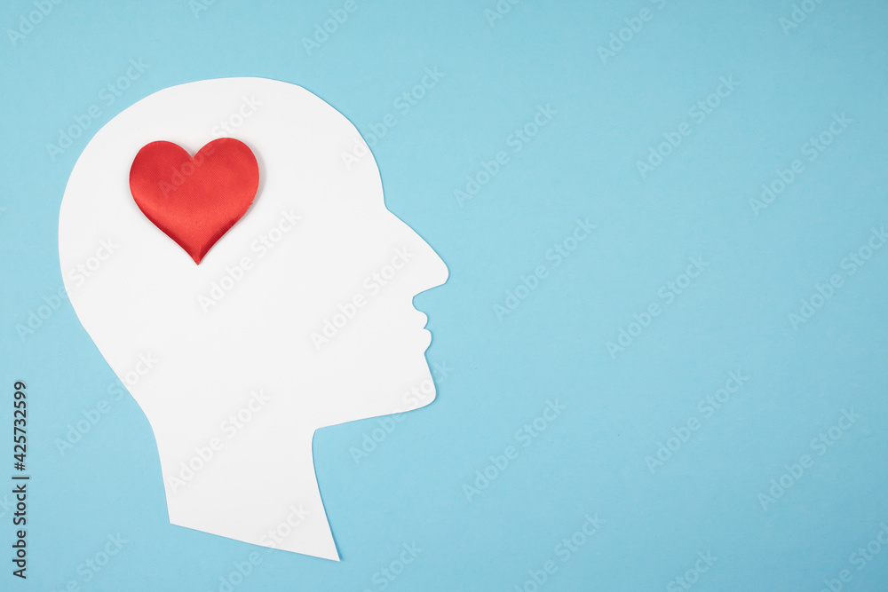 Paper silhouette of a head with a red heart on a blue background. Top view, place for text.
