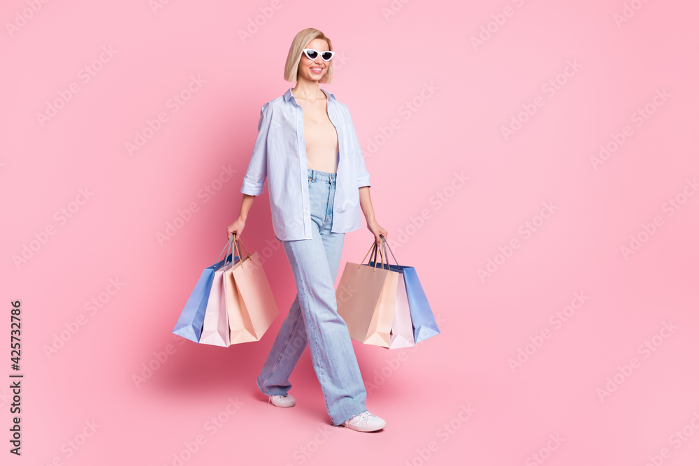 Full length photo of cheerful nice young woman walk hold shopping bags isolated on pastel pink color background Full length photo of cheerful nice young woman walk hold shopping bags isolated on pastel pink color background
