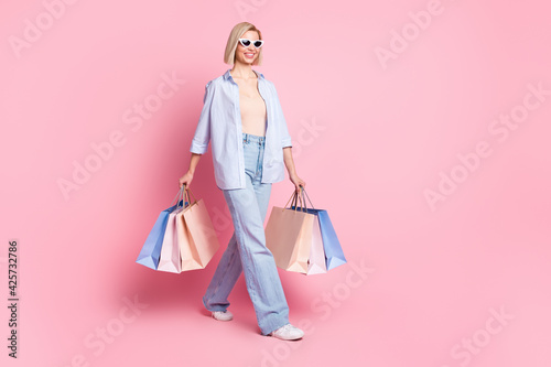 Full length photo of cheerful nice young woman walk hold shopping bags isolated on pastel pink color background