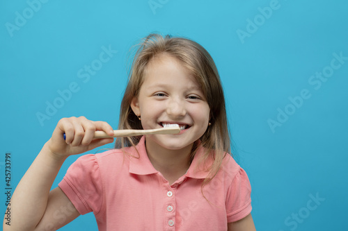 Dental concept. Close-up portrait of a pretty girl who brushes her teeth with an ecological brush on a blue background. Oral care, caries prevention.