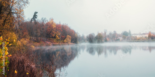 The village is in a fog. Panoramic view of morning haze over surface of the lake near Gatchina city