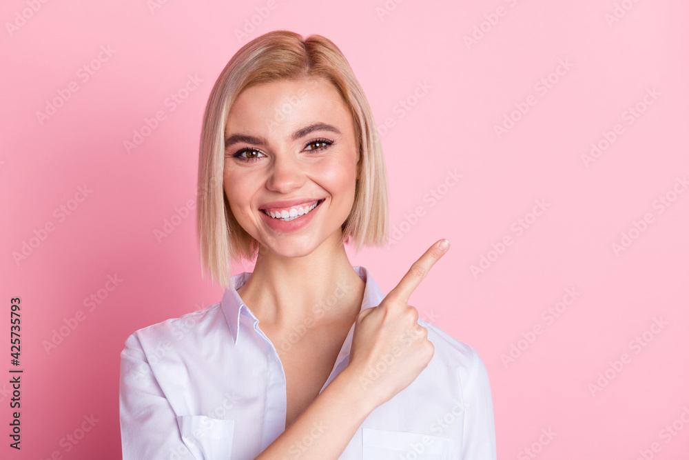 Photo of positive happy young woman smile point finger empty space promoter isolated on pastel pink color background Photo of positive happy young woman smile point finger empty space promoter isolated on pastel pink color background