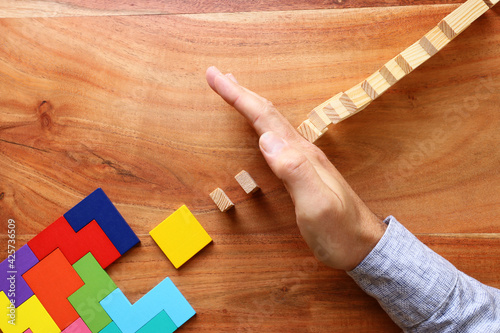 man's hand holding a square tangram puzzle, over wooden table