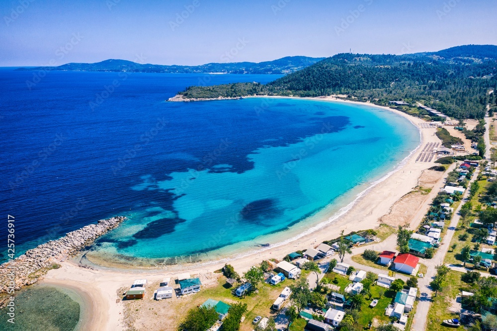 Beautiful Beach With Golden Sand And Clear Water. Turquoise coast with blue water and golden sand in Europe. Summer vacation background with turquoise sea water bay and pine trees aerial drone photo