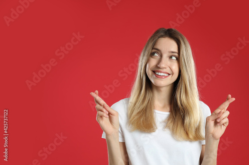 Woman with crossed fingers on red background, space for text. Superstition concept