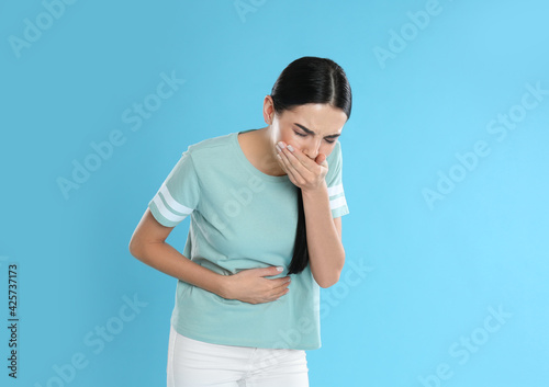 Woman suffering from stomach ache and nausea on light blue background. Food poisoning photo