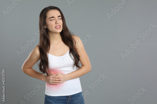 Young woman suffering from liver pain on grey background © New Africa