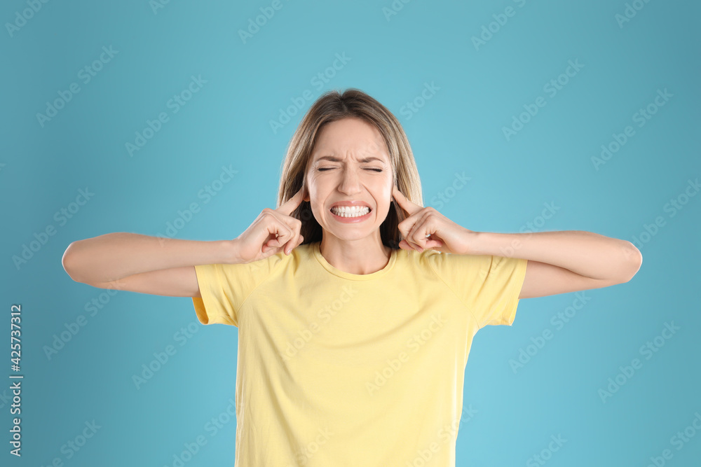 Emotional young woman covering her ears with fingers on light blue background Emotional young woman covering her ears with fingers on light blue background