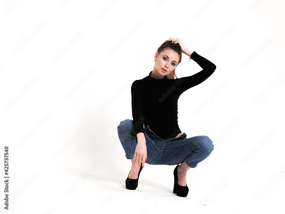 The brunette on a white background in a bodysuit and jeans with heels and a ponytail