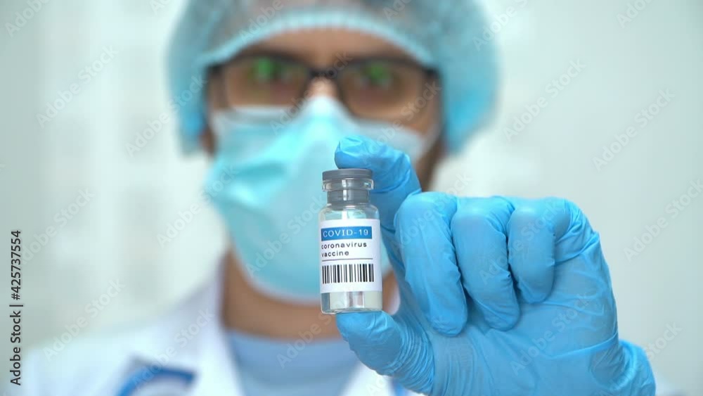 Close up of hand in medical glove holds amupla with vaccine covid-19 on background of male doctor in protective mask and white coat. Coronavirus vaccination Close up of hand in medical glove holds amupla with vaccine covid-19 on background of male doctor in protective mask and white coat. Coronavirus vaccination