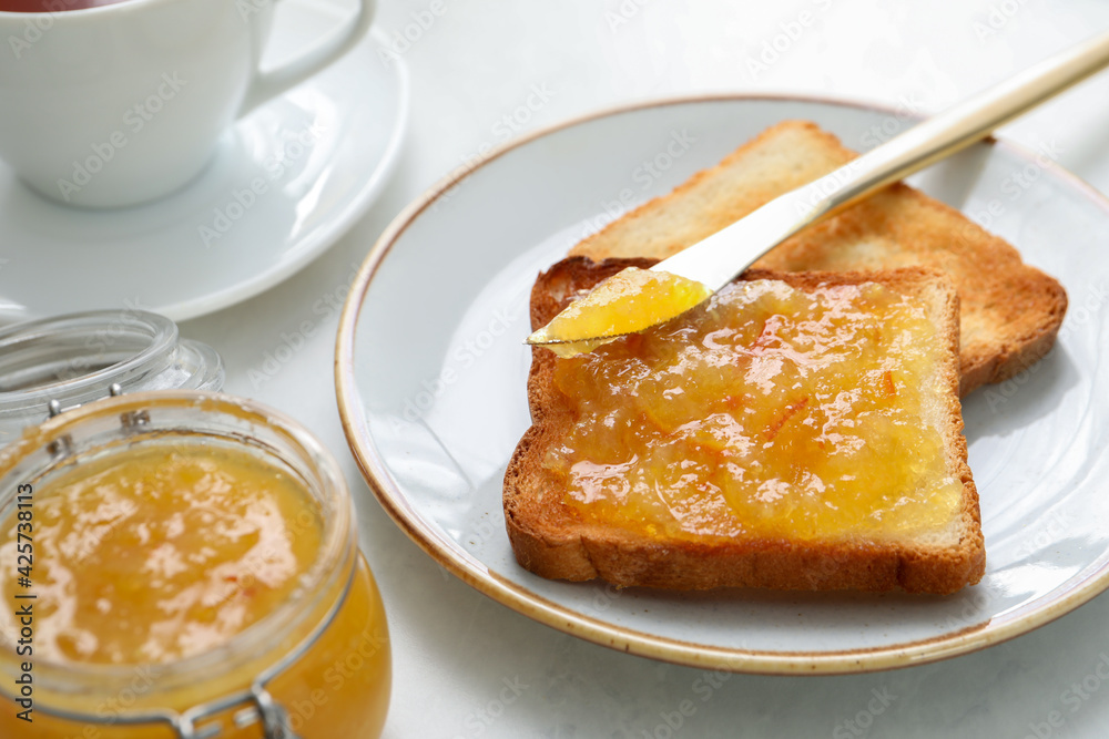 Delicious orange marmalade and toasts on white table, closeup