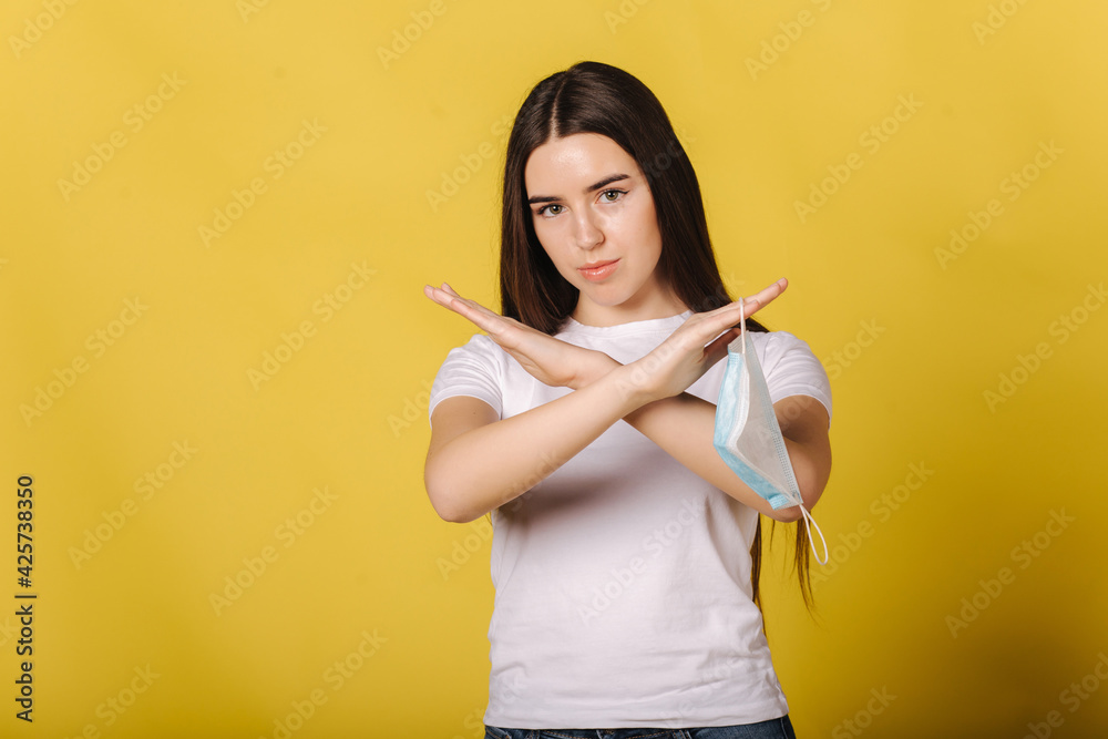 Attractive young woman hold protective mask in hand and think of its necessity. Female cross arms showing thet she won't wear a mask. Face mask it is the most useless thing in the world Attractive young woman hold protective mask in hand and think of its necessity. Female cross arms showing thet she won't wear a mask. Face mask it is the most useless thing in the world