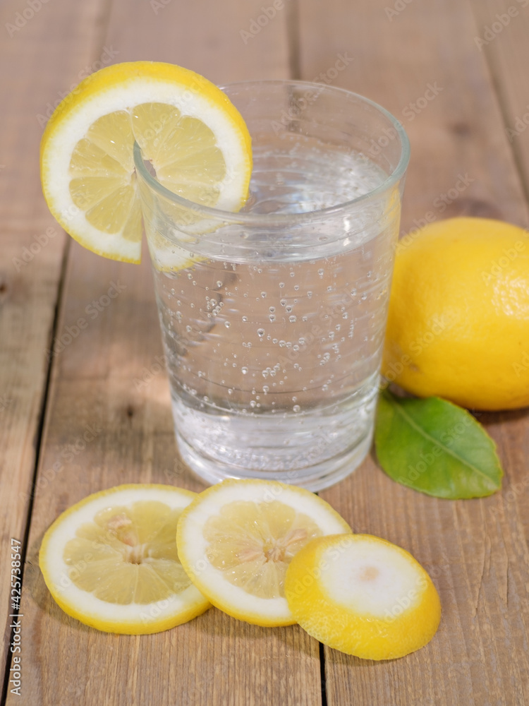 limone con foglia e bicchiere di vetro riempito con acqua frizzante e limone tagliato a fette, ricorda l'estate 