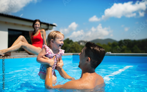 Young family with small daughter in swimming pool outdoors in backyard garden, playing. © Halfpoint