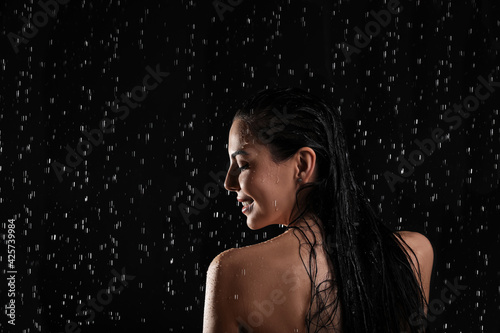 Pretty woman taking shower on black background. Washing hair