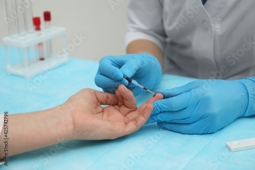 Doctor taking blood sample from patient's finger at table in clinic, closeup
