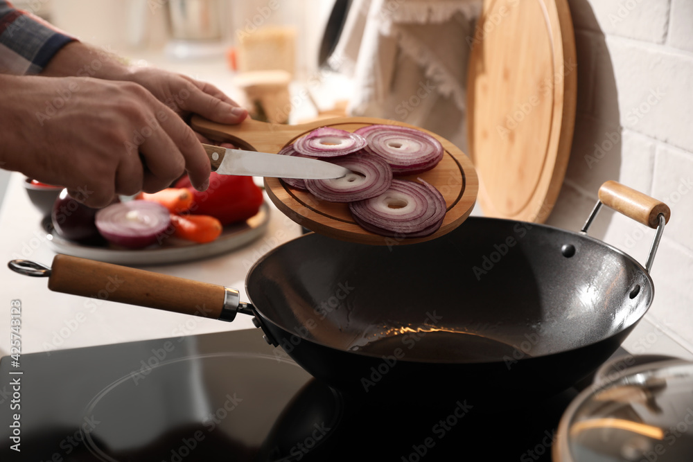 Man pouring onion slices into frying pan, closeup