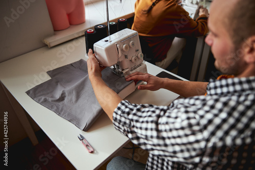 Male tailor sewing grey cloth with a machine