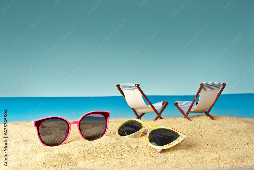Pink glasses on the sand close up. Glasses on a beach chair background. Beach chairs on a background of blue water and sky. Summer, sea and vacation concept.