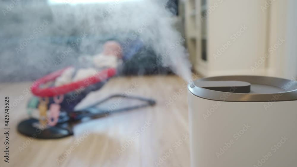 working ultrasonic humidifier adds moisture into dry air in living room with newborn baby boy in rocking chair. High quality 4k footage working ultrasonic humidifier adds moisture into dry air in living room with newborn baby boy in rocking chair. High quality 4k footage