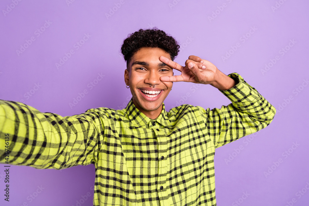 Photo portrait of guy showing v-sign gesture like taking selfie in plaid shirt isolated on pastel purple color background Photo portrait of guy showing v-sign gesture like taking selfie in plaid shirt isolated on pastel purple color background