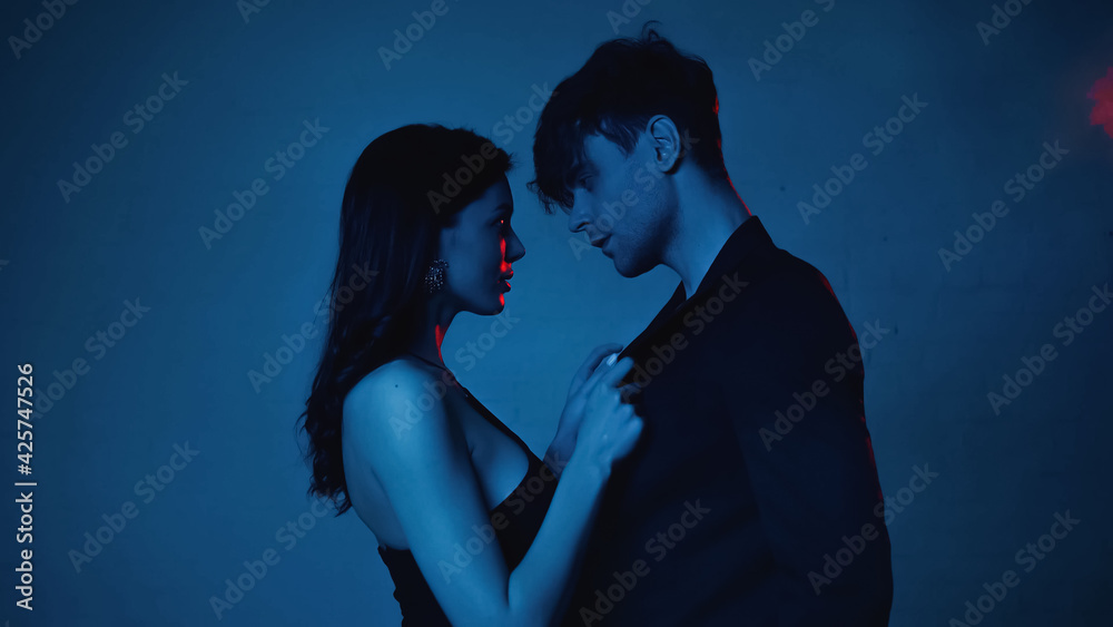 side view of seductive woman touching blazer of boyfriend on blue
