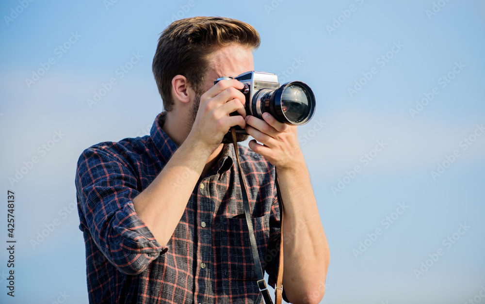 Obraz premium Reporter taking photo. Manual settings. Travel blogger. Vintage equipment. Hipster photographer. Blogger shooting vlog. Guy outdoors blue sky background. Handsome blogger guy traveler retro camera