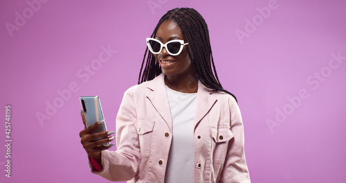 Pretty African American woman doing selfie shot on mobile phone isolated over pink background. © VAKSMANV