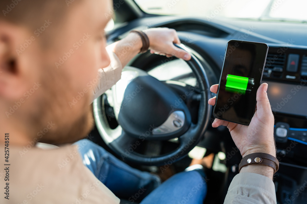 Man watching electric car charge indicator through smartphone app. Battery level on the mobile phone screen
