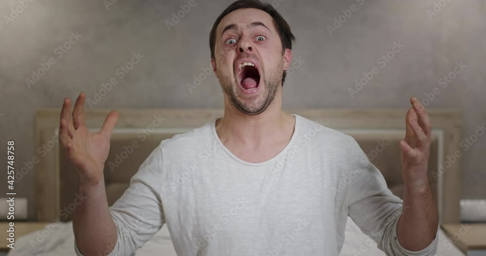 Nervous breakdown crazy nervous man screaming aggressively gesturing with hands at home sitting on bed emotional actor