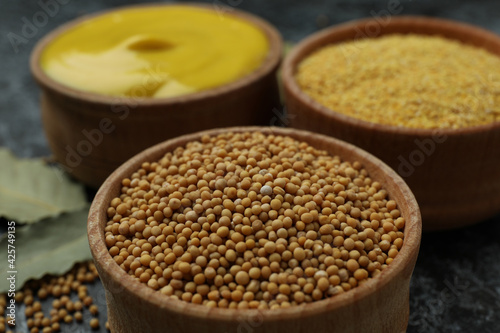 Wooden bowls with mustard seeds, sauce and powder, close up